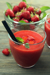 Glasses of strawberry smoothie with berries on table close up
