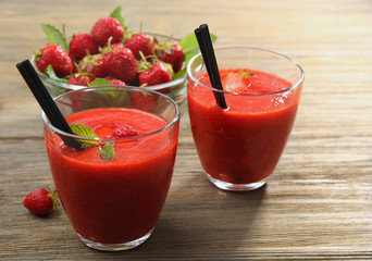 Glasses of strawberry smoothie with berries on table close up
