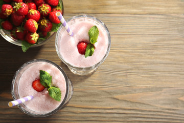 Glasses of milkshake with strawberries on wooden table close up