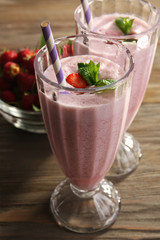 Glasses of milkshake with strawberries on wooden table close up