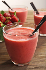 Glasses of milkshake with strawberries on wooden table close up