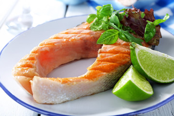 Tasty grilled salmon with greens on table close up