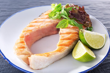 Tasty grilled salmon with greens on table close up
