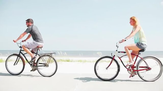 A young couple cycles down the beachfront on classic bicycles