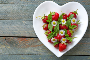 Red ripe strawberries on heart shaped plate, on color wooden background