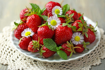 Red ripe strawberries on plate, on color wooden background
