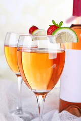 Glasses of wine with strawberries and slice of lime on light background