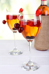 Glasses of wine with berries on light blurred background