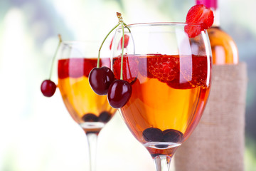 Glasses of wine with berries on light blurred background