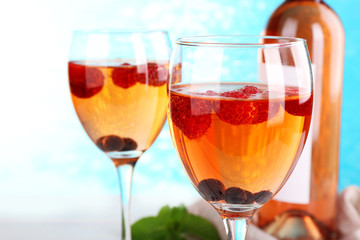 Glasses of wine with berries on light blurred background
