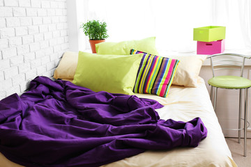 Comfortable bed with colorful pillows and purple blanket in bedroom