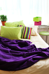 Comfortable bed with colorful pillows and purple blanket in bedroom