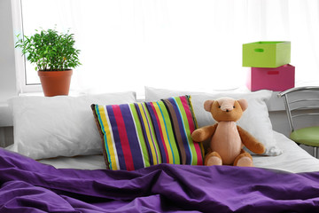 Comfortable bed with teddy bear in bedroom