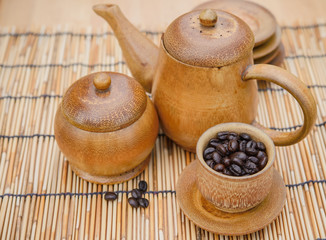 Coffee beans, cup of coffee and teapot on bamboo wooden desk. Se