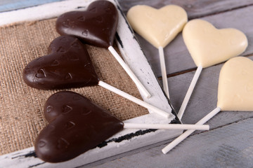 Chocolate heart shaped candies on sticks on wooden table, closeup