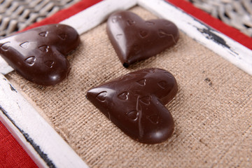 Chocolate heart shaped candies on sticks on frame with sackcloth, closeup