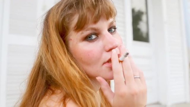 Young woman sits on a porch and smokes
