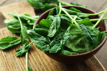 Bowl of fresh spinach leaves on wooden cutting board, closeup