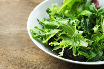 Bowl of mixed green salad on wooden table, closeup