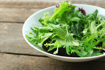 Bowl of mixed green salad on wooden table, closeup