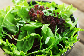 Bowl of mixed green salad on wooden table, closeup