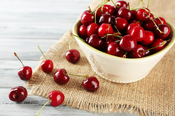 Fresh cherries in bowl with sackcloth on wooden table, closeup