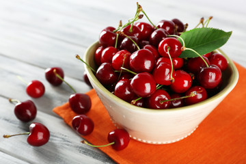 Fresh cherries in bowl with napkin on wooden table, closeup