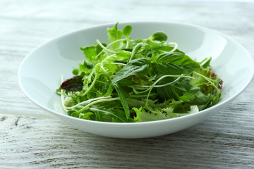 Fresh mixed green salad in bowl on wooden table close up