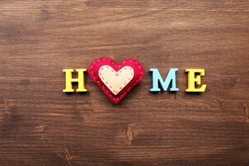 Decorative letters forming word HOME with heart on wooden background