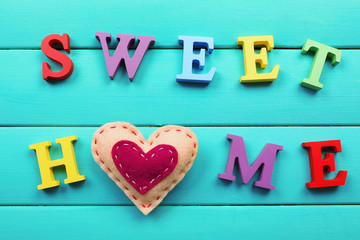Decorative letters forming words SWEET HOME with heart on wooden background