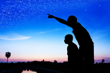 Silhouette of father use hand point his son look at meteor showe