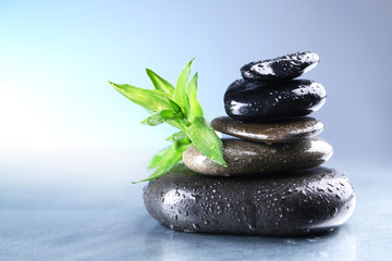 Stack of wet spa stones with green leaves on light blue background