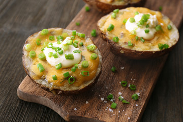 Baked potato with mayonnaise and chives on wooden cutting board, closeup
