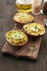 Baked potato with mayonnaise and chives on wooden cutting board, closeup