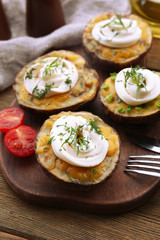 Baked potato with mayonnaise and herbs on wooden cutting board, closeup