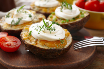 Baked potato with mayonnaise and herbs on wooden cutting board, closeup
