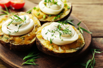 Baked potato with mayonnaise and herbs on wooden cutting board, closeup