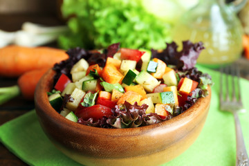 Wooden bowl of fresh vegetable salad on napkin, closeup