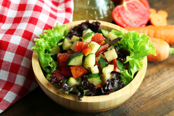 Wooden bowl of fresh vegetable salad on wooden table, closeup