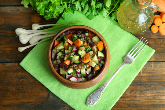 Wooden bowl of fresh vegetable salad on napkin, top view