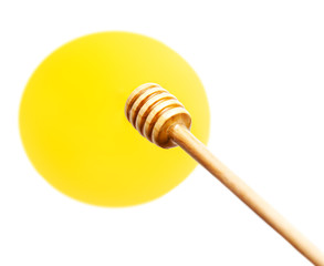 Wooden honey dipper with yellow honey flowing drops isolated on