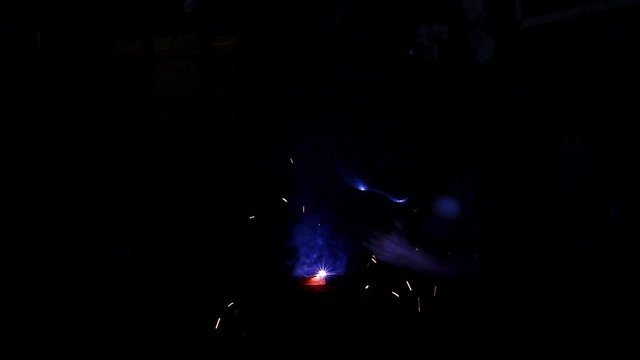 Arc welder with welding sparks. Flashes and lot of sparks from welding work at dark in workshop.
