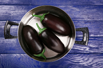 Fresh eggplant in pan on wooden table, top view