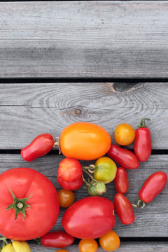 Different variety of tomatoes on grey timber planks.