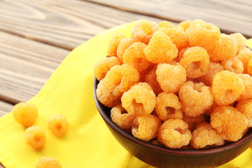 Bowl of yellow raspberries on wooden table with yellow napkin, closeup