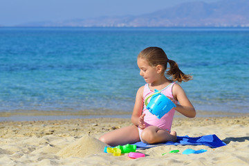Adorable toddler girl playing with her toys at the beach