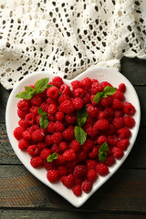 Sweet raspberries on plate, on wooden  background
