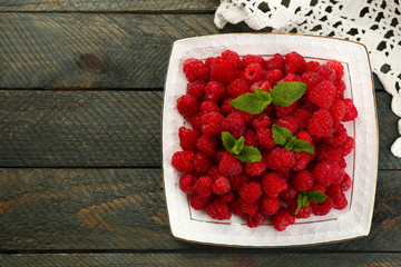 Sweet raspberries on plate on wooden  background