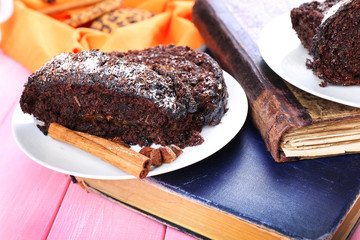 Delicious chocolate roll in saucer with spices on wooden table near book, closeup