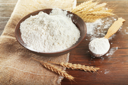 Bowl of whole flour with wheat ears on wooden table, closeup